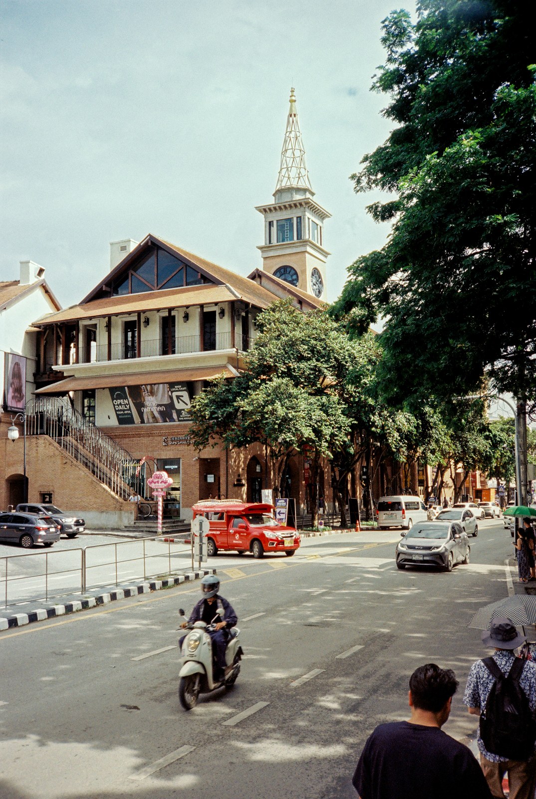 A church spire on a street corner, a scooter passing